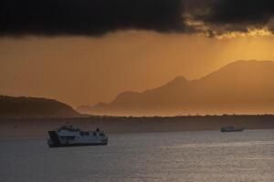 Two passenger ships sailing in the Bali Strait with the background of the cloudy sunrise and the silhouette of mountain formations. photo