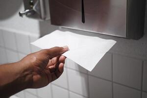 A Hand Extending Toward a Paper Towel from the Dispenser in the Restroom photo