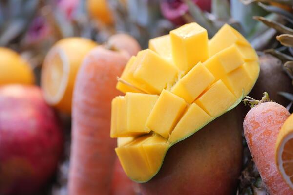 A colorful display featuring a variety of mangoes, apples, carrots, and other produce.