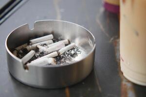 An ashtray containing cigarettes situated next to a refreshing beverage photo