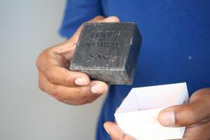 Hand gently holding a bar of black soap placed in an open box photo