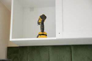 A power drill is stored neatly on a shelf within a modern kitchen cabinet photo
