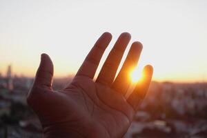 A Hand Extending Gracefully Towards the Bright Sunlight Shining Above the Urban Cityscape Below photo
