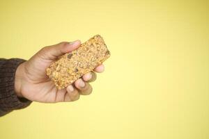 A Hand Gently Holding a Delicious Granola Bar Against a Bright Yellow Background photo