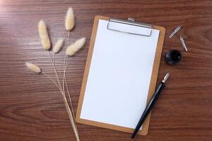 Blank clipboard with dip pen and dried grass on wooden texture background. photo