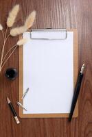 Blank clipboard with dip pen and dried grass on wooden texture background. photo
