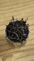 A Collection of Dried Tea Leaves Resting in a Metal Scoop on a Smooth Wooden Surface photo