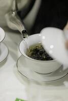 A teapot gracefully pouring aromatic tea into a pristine white ceramic cup for enjoyment photo