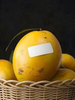 A blank white sticker mockup is attached to a yellow ripe mango kept in a basket photo