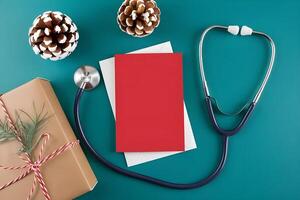 A blank red Christmas card mockup is placed on a doctor table along with stethoscope and gift photo
