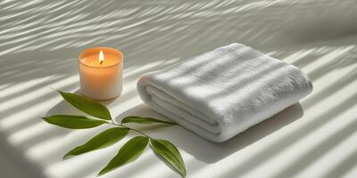 A rolled white towel, lit candle, and a single leaf placed on a spa bed photo