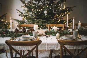Christmas table setting decorated with candles, pine cones, and greenery with christmas tree in background photo