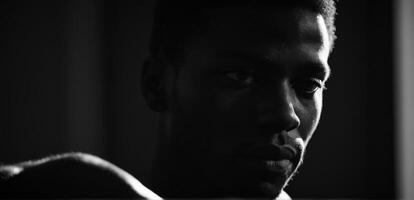A black man is looking at the camera in a dark room photo