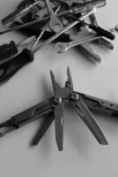Folding utility multi-tool with opened blades against a bunch of unnecessary tools monochrome stock image photo