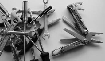 Black and white image of blades and screws of steel multi-tool VS pile of hand tools dumped in disarray photo