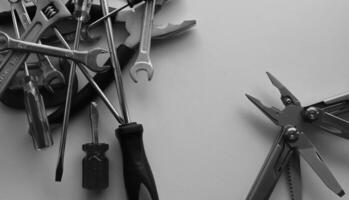Grayscale image of opened multi tool and a stack of variety tools on white workbench photo