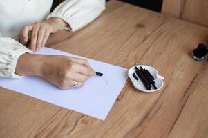 Woman Practicing Calligraphy with Black Ink and Nibs on White Paper photo