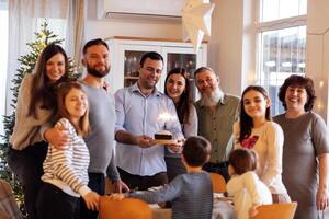 A big happy family at a festive table at home. An attractive young man with a cake with lighted sparklers and his smiling relatives in the living room. photo