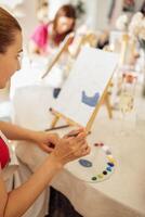 A female hands with a brush and a palette with paints. The artist mixes acrylic paints. A woman paints on canvas at an easel at a table in the workshop. photo