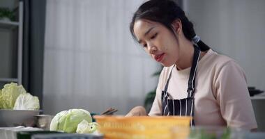 Handheld shot, Happy young woman cutting cabbage on the table to prepare to make sukiyaki or shabu-shabu hot pot at home. Food preparation video