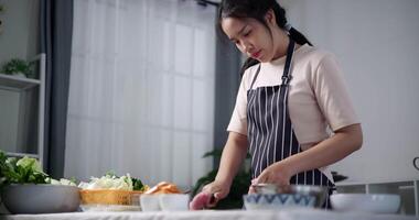 Handheld low angle view shot, Happy young woman is slicing pork on the table to prepare to make sukiyaki or shabu shabu hot pot at home. Food preparation video