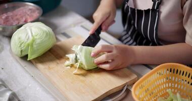 Handheld selective focus shot, Happy young woman cutting cabbage on the table to prepare to make sukiyaki or shabu-shabu hot pot at home. Food preparation video