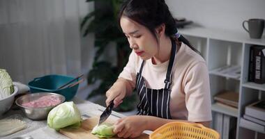 Handheld high angle view shot, Happy young woman cutting cabbage on the table to prepare to make sukiyaki or shabu-shabu hot pot at home. Food preparation video