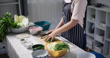 Handheld selective focus shot, Happy young woman cutting vegetables on the table to prepare to make sukiyaki or shabu-shabu hot pot at home. Food preparation video