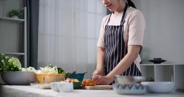 Handheld low angle view shot, Happy young woman is slicing sausage on the table to prepare to make sukiyaki or shabu shabu sukiyaki at home. Food preparation video