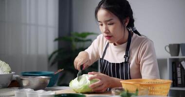 Handheld shot, Happy young woman cutting cabbage on the table to prepare to make sukiyaki or shabu-shabu hot pot at home. Food preparation video