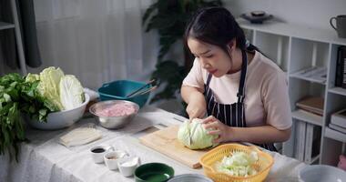 Handheld high angle view shot, Happy young woman cutting cabbage on the table to prepare to make sukiyaki or shabu-shabu hot pot at home. Food preparation video