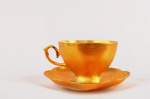 A golden tea cup with a saucer on a pink background. photo