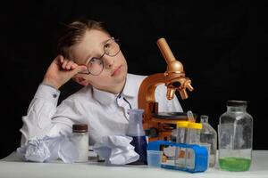 A boy scientist researcher with a microscope is thinking about ideas in the laboratory. Surprise in the laboratory. Science and education. photo