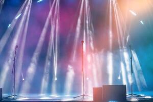 Blurred rays of light from stage spotlights on a multi-colored stage background with microphones. The beginning of a concert or show. photo