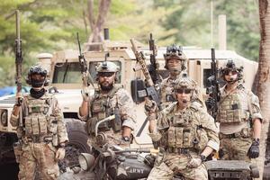 Portrait of soldiers in camouflage uniforms hold weapons in front of a military communication vehicle photo