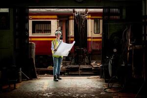 Portrait of railway technician worker in safety vest and helmet working with blueprint at train repair station photo