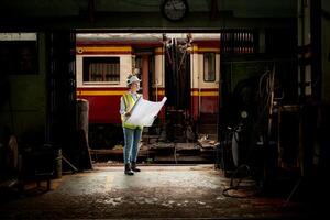Portrait of railway technician worker in safety vest and helmet working with blueprint at train repair station photo