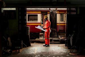 Portrait of railway technician worker in safety vest and helmet working with blueprint at train repair station photo