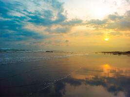 A mesmerizing sunset where the golden hues of the sun and the sky reflect perfectly on the wet, glistening sand along the shore photo