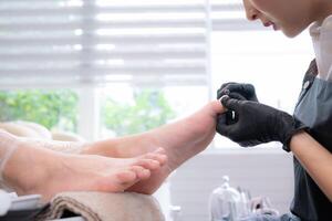 A nail technician is using tools to cut and polish foot of a customer. photo