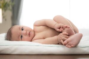 A tiny child smiles happily on the bed waiting for mother apply powder and put on clothes after taking a bath photo