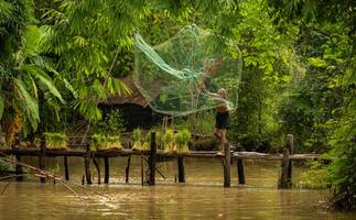 Fisherman atop the bridge netting fish in the river with a fishnet photo