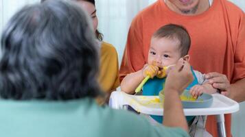 un pequeño niño comiendo su primero comida, padres y abuelos animar emocionado foto