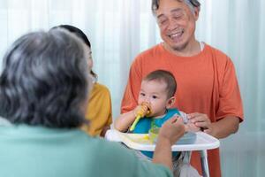 un pequeño niño comiendo su primero comida, padres y abuelos animar emocionado foto