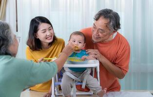 un pequeño niño comiendo su primero comida, padres y abuelos animar emocionado foto