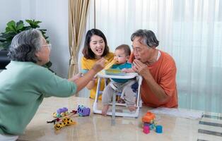 un pequeño niño comiendo su primero comida, padres y abuelos animar emocionado foto