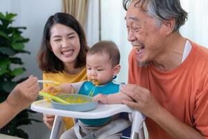 un pequeño niño comiendo su primero comida, padres y abuelos animar emocionado foto