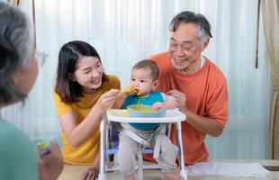 un pequeño niño comiendo su primero comida, padres y abuelos animar emocionado foto