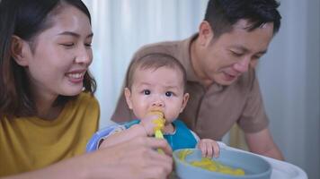 un pequeño niño comiendo su primero comida, padres animar emocionado foto