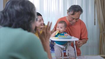 un pequeño niño comiendo su primero comida, padres y abuelos animar emocionado foto